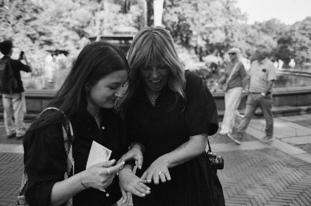 A couple looks down at the engagement ring with matching awe and laughter, captured in black and white moments after their Central Park proposal.
