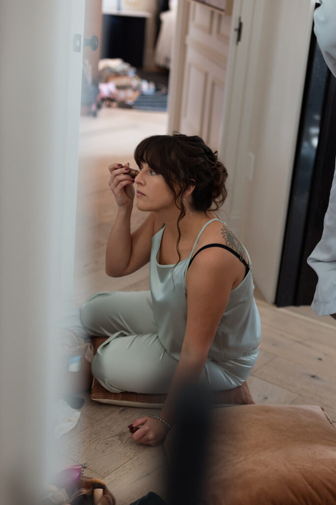 Bridemaid applies her makeup while sitting on hotel floor.