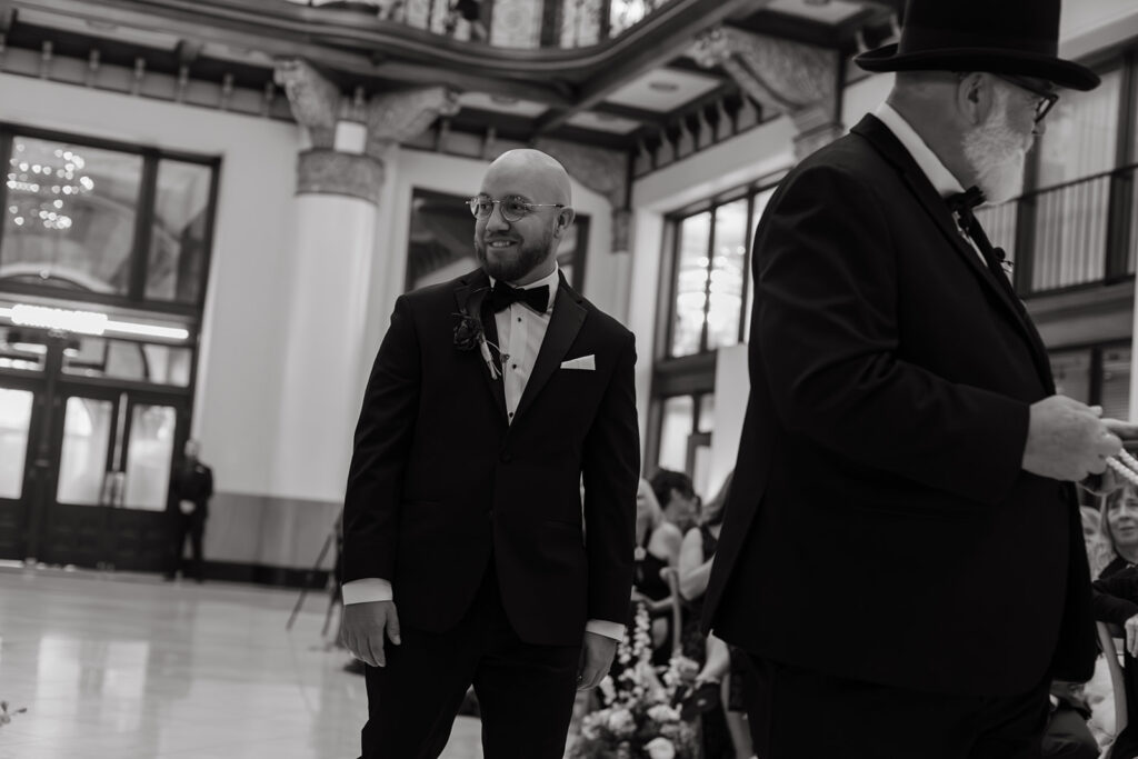 Groom walks down the aisle as documentary wedding photographer captures him sharing a glance with a wedding guest.