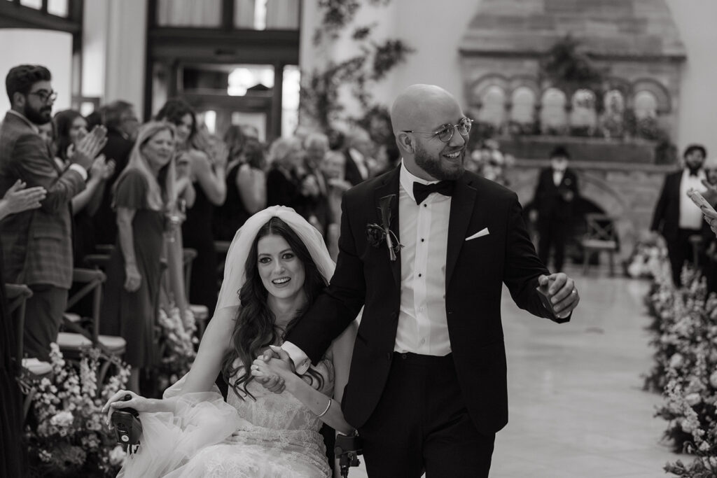 Fiona Cauley walks down the aisle hand in hand with her husband while guests cheer.
