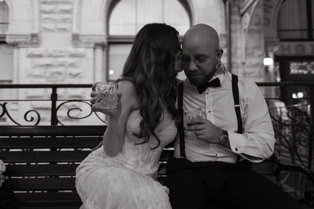 Newlyweds share a cocktail and a quiet moment on a bench, as captured by their documentary wedding photographer. 