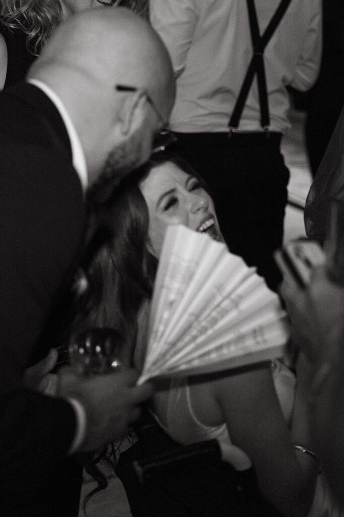 Documentary wedding photographer captures groom fanning off bride Fiona Cauley as she throws her head back in laughter during their Union Station reception in Nashville