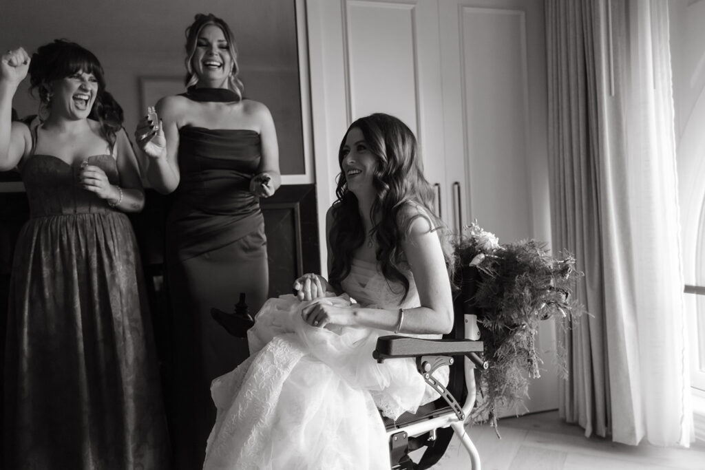 Bride laughs as bridesmaids surround her wheelchair and cheer.
