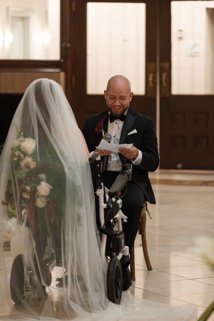 Groom grins as he sits to read vows to his wife during their Union Station wedding, as captured by documentary wedding photographer Ali Miller.