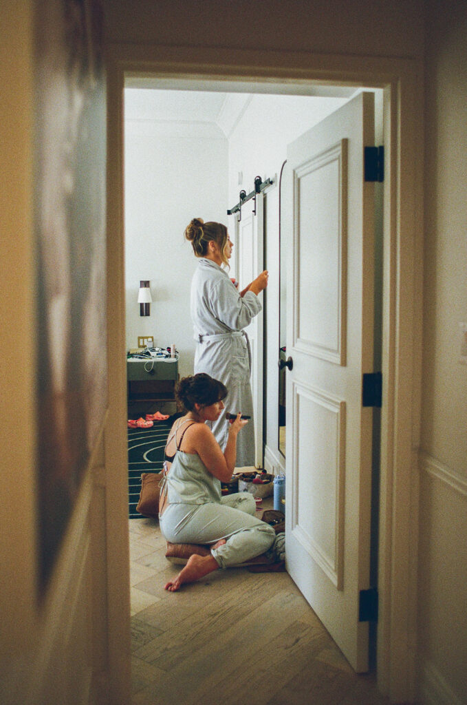 Documentary wedding photographer captures bridesmaids getting ready through the hotel room door.
