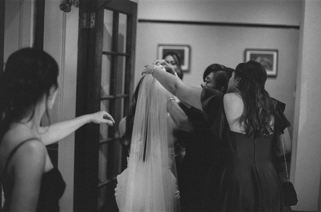Emotional candid photo of bride's sisters and mom gathered around to fix her veil 