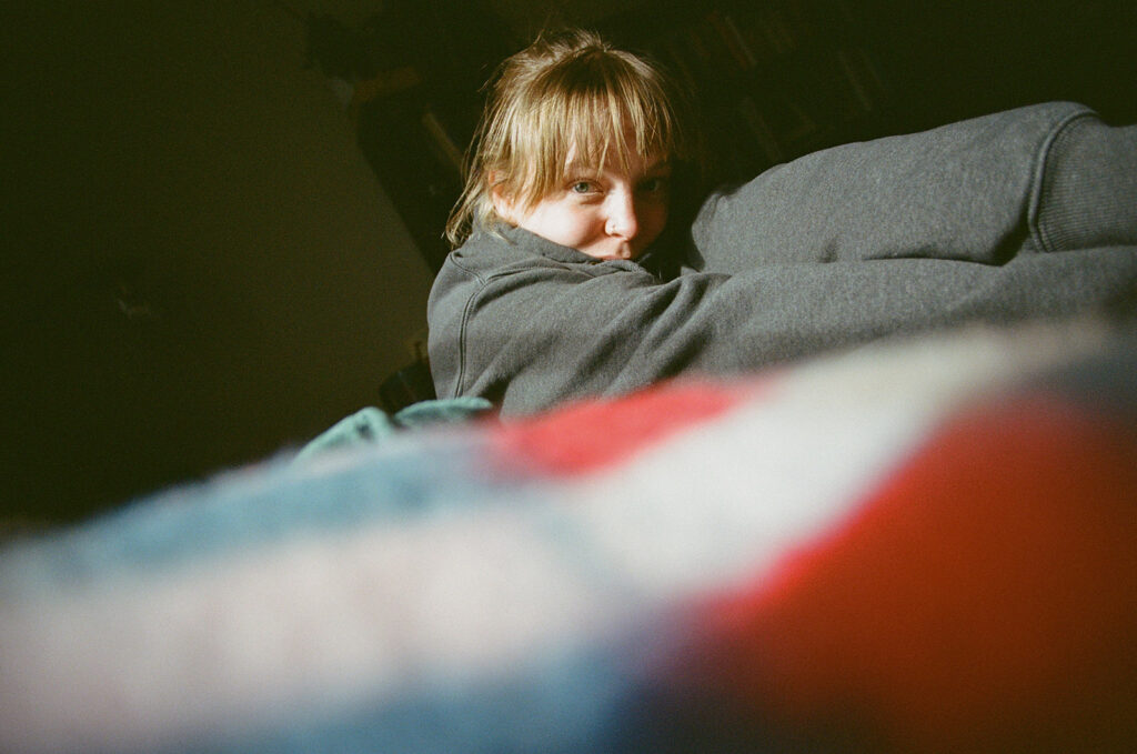 Candid portrait of Nashville photographer Ali Miller peeking over the back of a couch during an in-home documentary photography session.