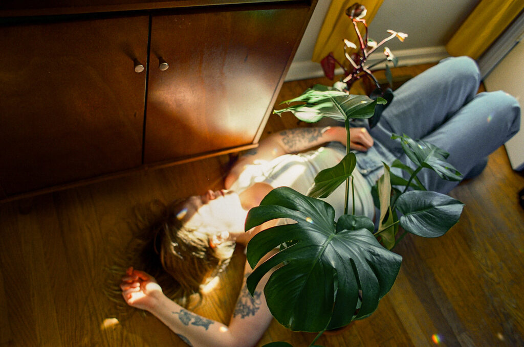 Documentary-style branding photograph of Nashville photographer Ali Miller resting on the floor beside a sunlit monstera plant.
