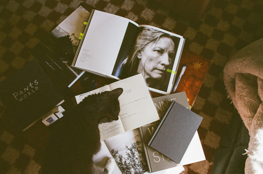 Overhead documentary photograph of Ali Miller's coffee table filled with books, notebooks, film, and everyday objects that reflect her creative life.