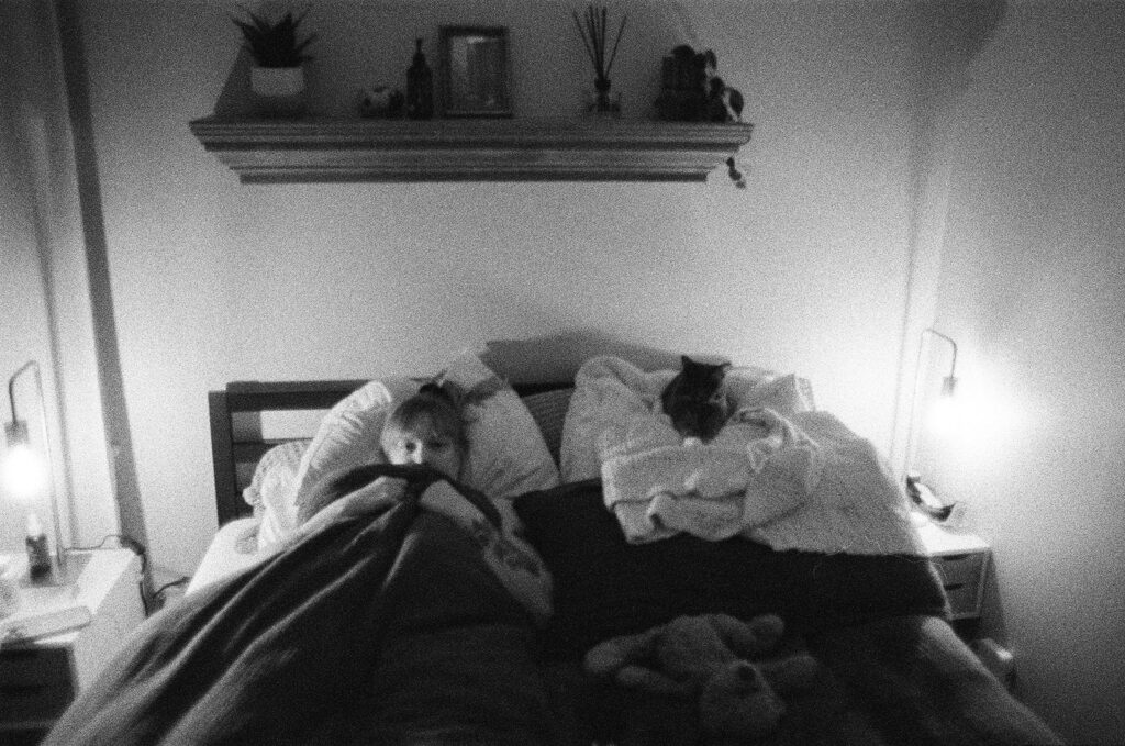 Documentary-style photograph of Nashville photographer Ali Miller relaxing in bed beside her cat, Minerva, at the end of the day.