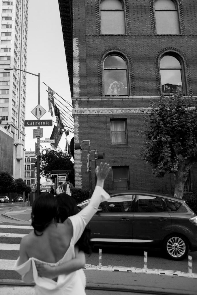 Lesbian brides in downtown San Francisco wave at a passing car