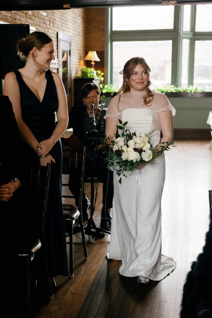 Friend of bride looks at her adoringly as she makes her way down the aisle at Saint Paul wedding
