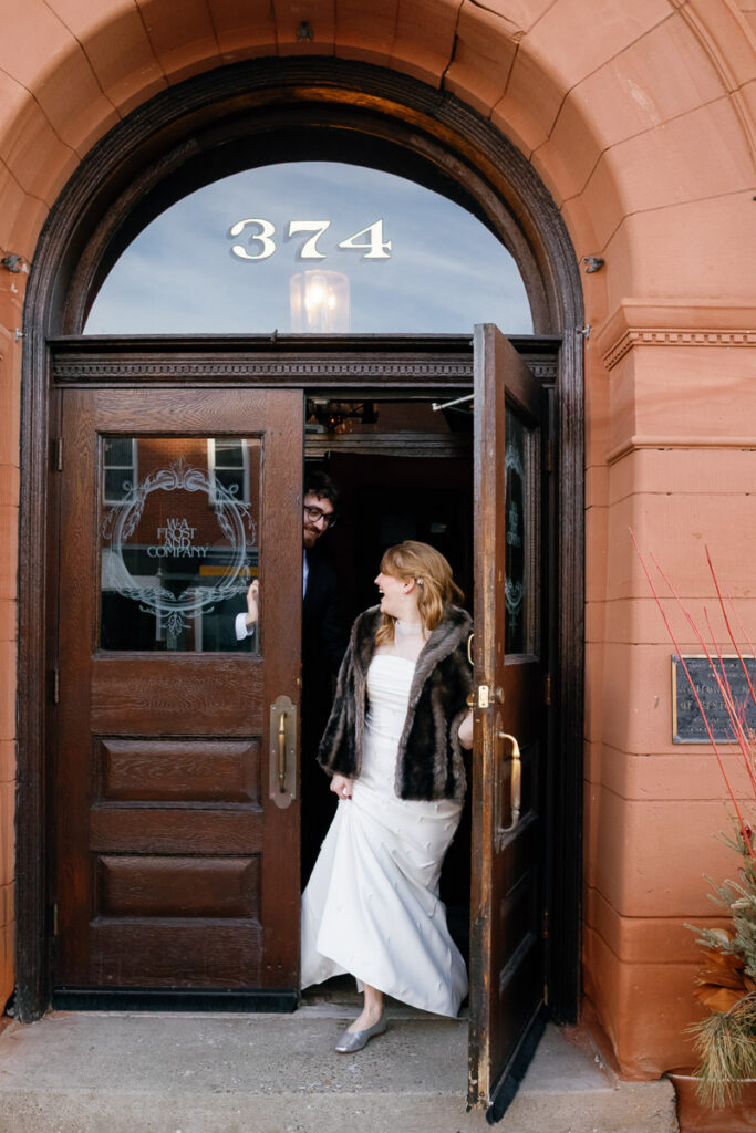 Candid wedding photography captures bride and groom walking out the arched doorway of WA Frost and Co. in Saint Paul, Minnesota