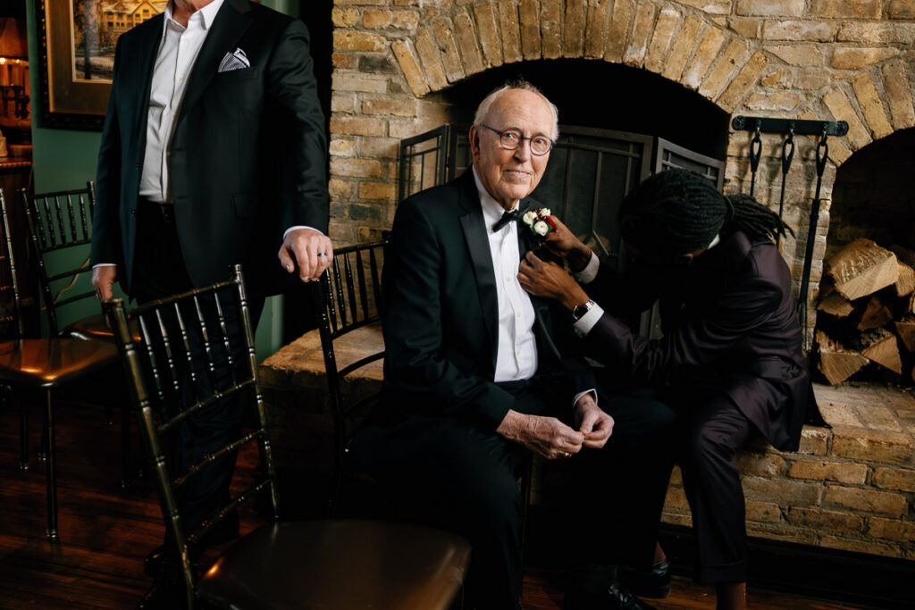 Wedding guest helps pin flowers on grandfather's tuxedo jacket in emotional candid wedding photo
